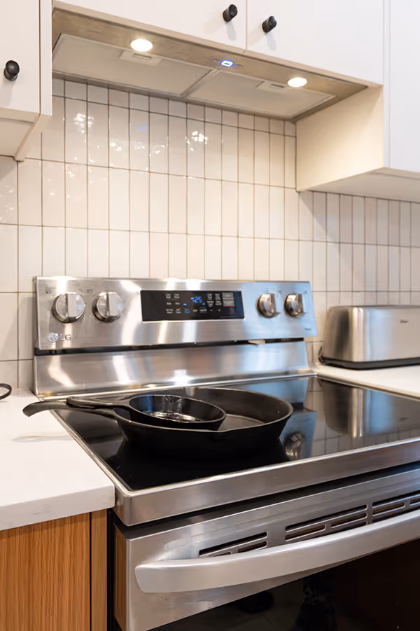 Modern kitchen stove with two cast iron skillets on a black ceramic cooktop beneath white cabinets and a tiled backsplash.