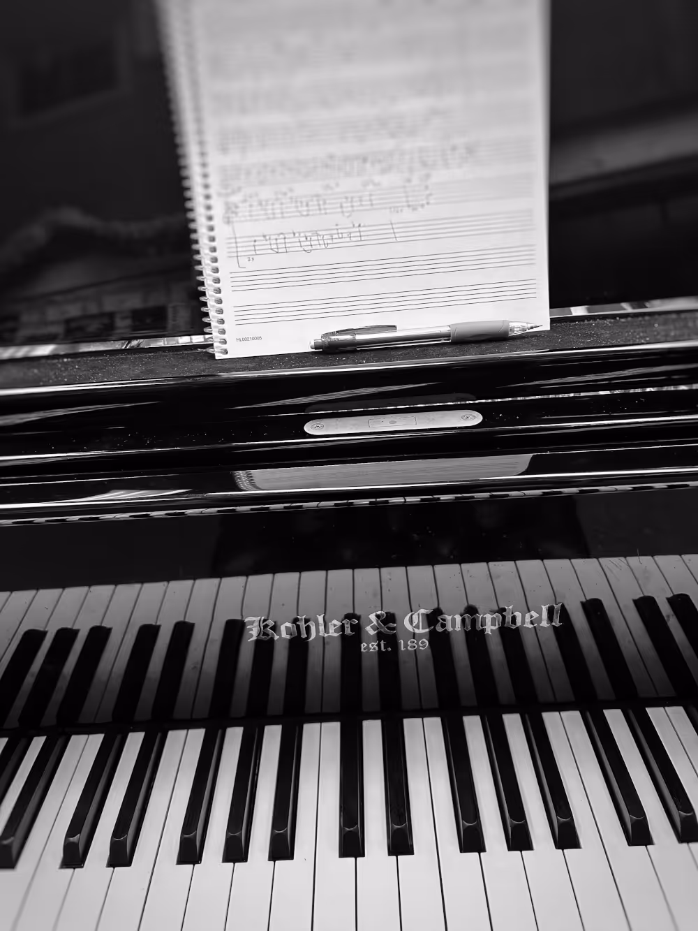 Close-up of piano keys with sheet music and a pen on the music stand.