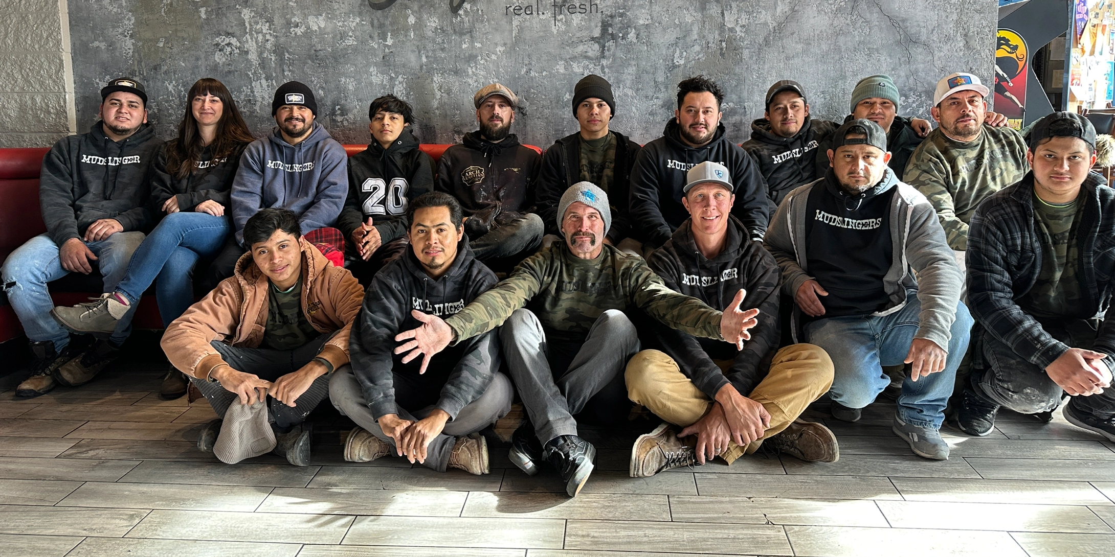 Several men sitting in front of a textured wall looking at the camera