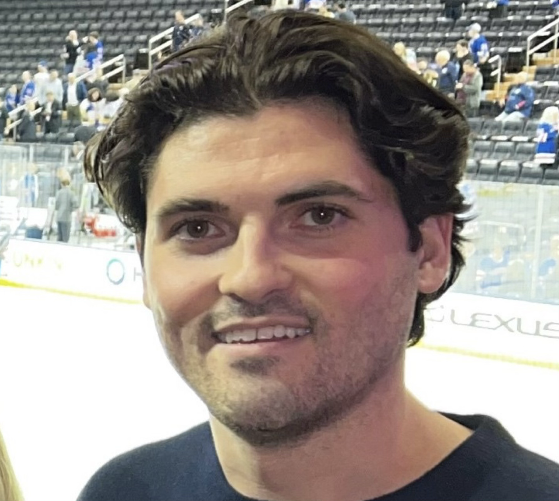 Mason Corliss with dark wavy hair and light facial hair smiling at an indoor ice hockey arena.