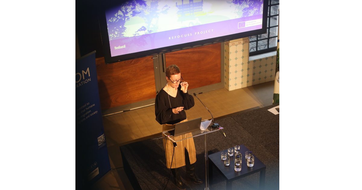 Congreszaal met podium, blauwe en paarse lichtbundels, en een grote verlichte letter A.