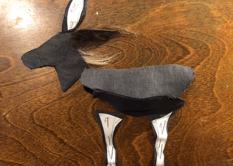 A fabric donkey craft piece with black and gray cloth sections, attached to a wooden surface.