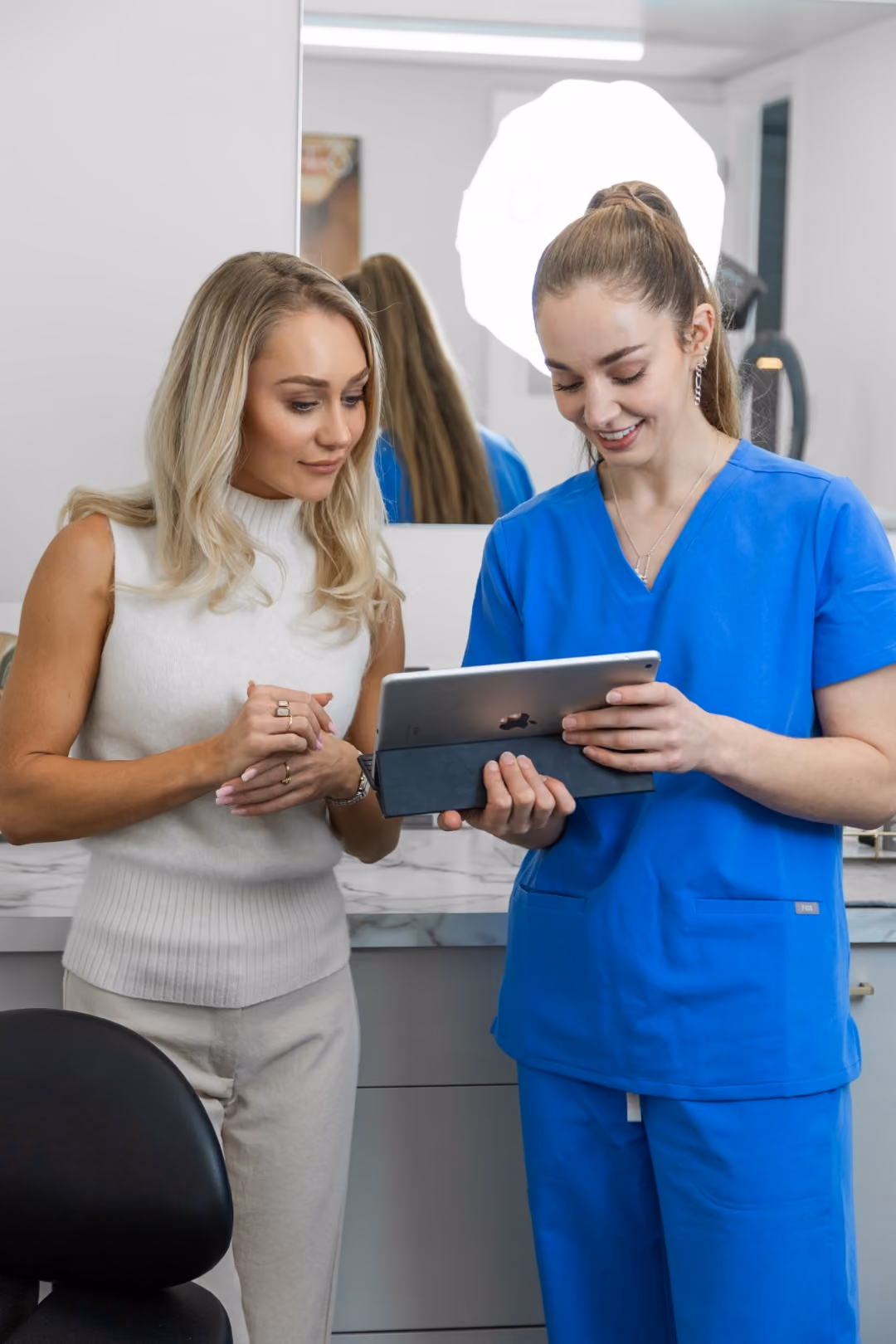 Practitioner in blue scrubs talking a client through her treatment plan on a tablet