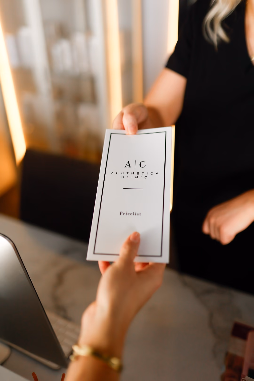 Aesthetica Clinic price list being handed to a client across the reception counter