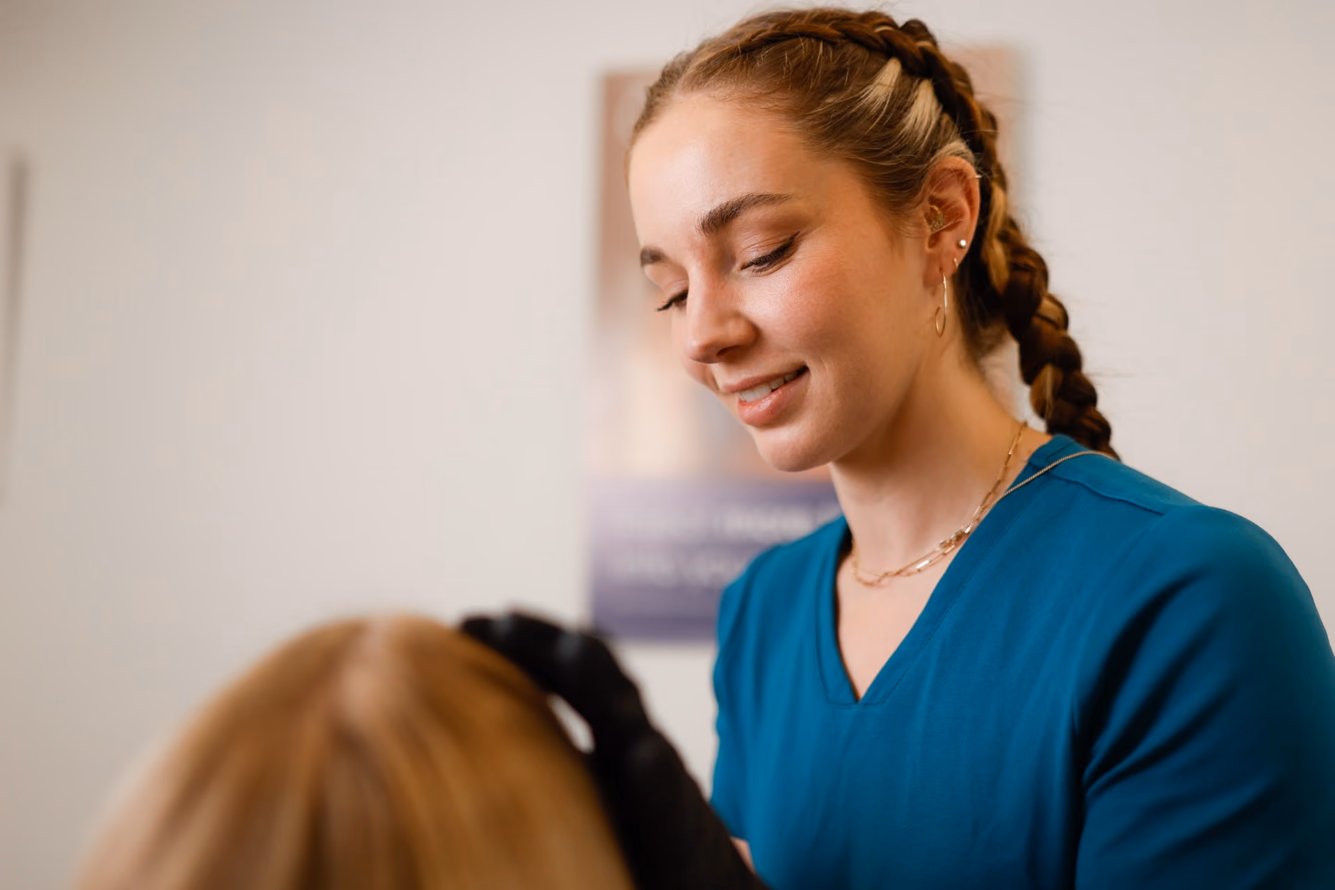 Aesthetica Clinic practitioner in teal scrubs smiling while treating a client