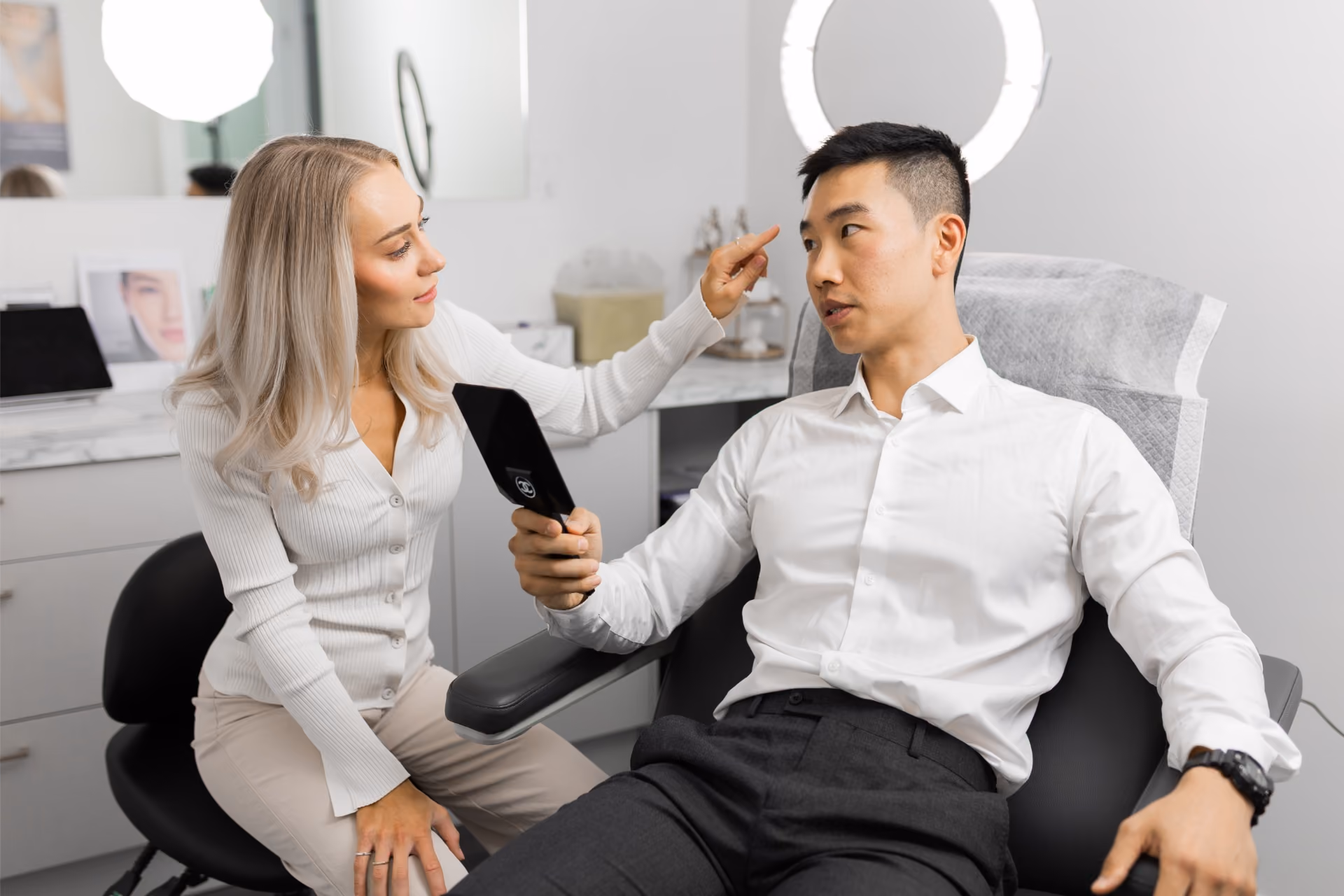 Practitioner assessing a client's face during a consultation while he holds a hand mirror