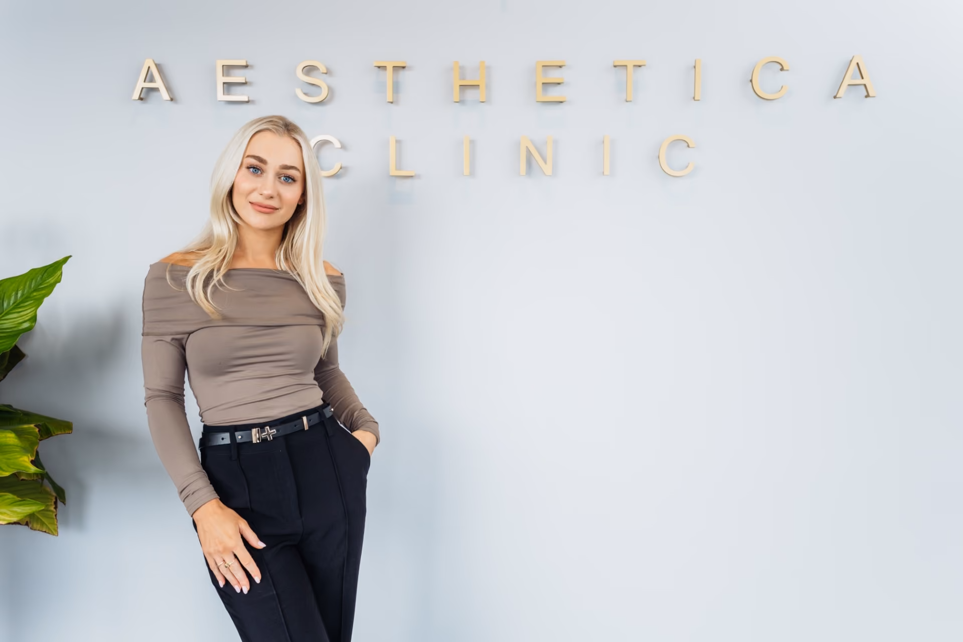 Clinician standing in front of the gold Aesthetica Clinic sign in the Christchurch clinic