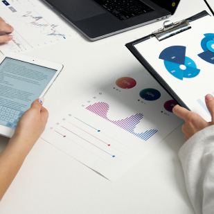 Personas analizando gráficos y datos con tablet, laptop y documentos sobre una mesa blanca.