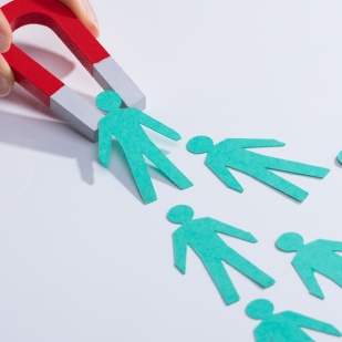 Imán rojo atrayendo una figura de papel de persona entre varias figuras similares sobre fondo blanco.