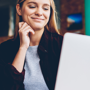 Mujer sonriendo mientras usa una computadora portátil blanca.