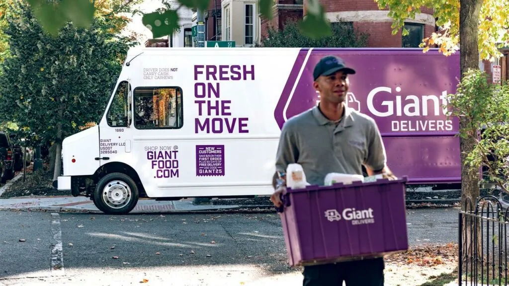 Giant Delivers driver carrying groceries beside a branded delivery truck.