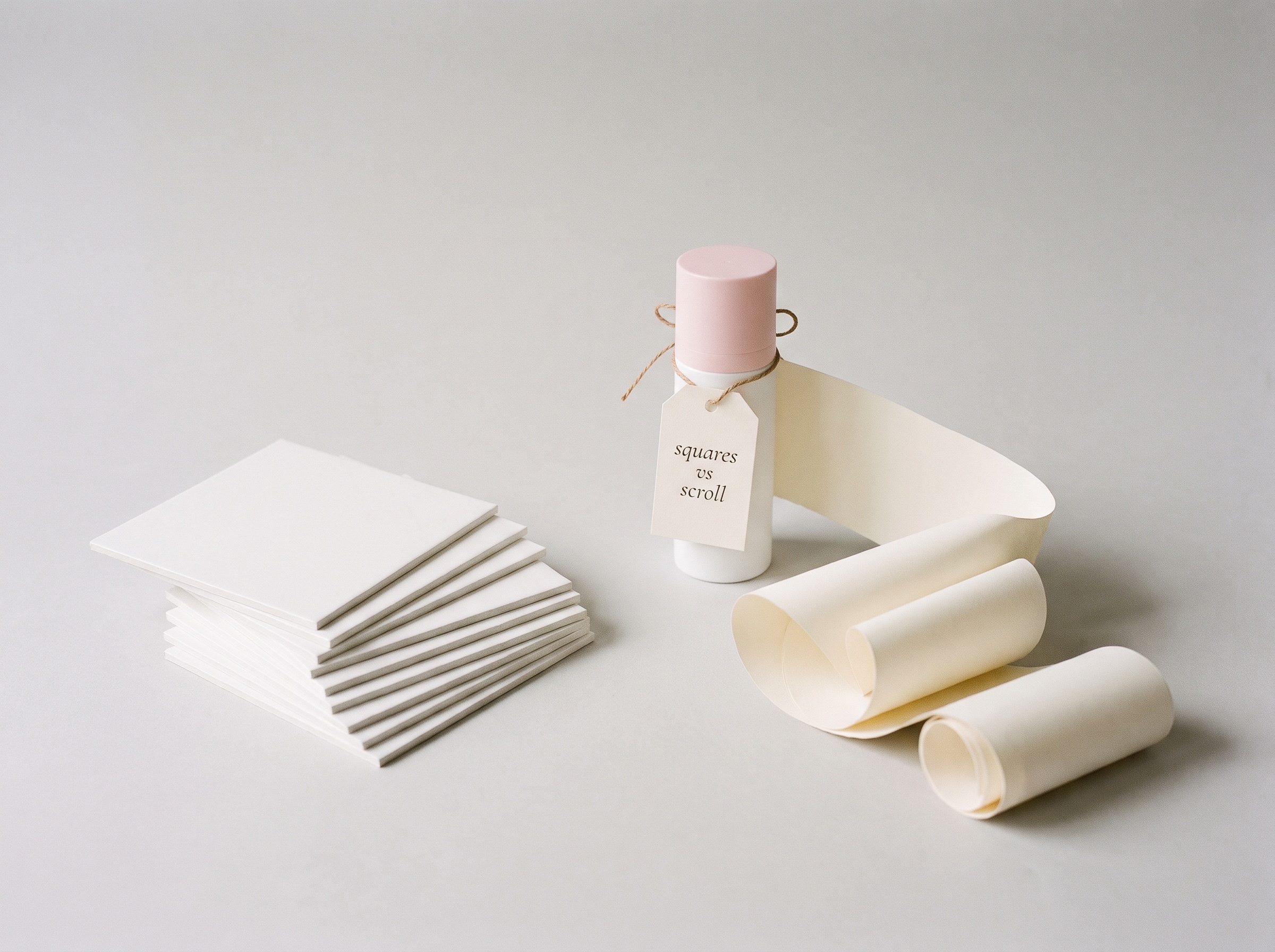 Stack of square white cards beside a skincare bottle unrolling a long paper scroll, tagged squares vs scroll