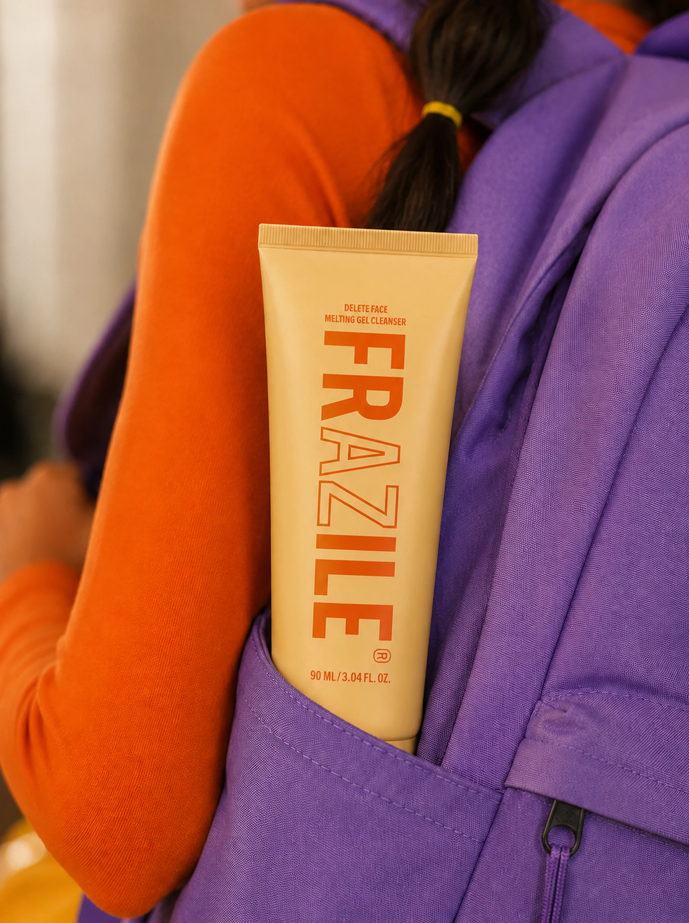 FRAZILE cleanser tube styled inside a purple backpack beside an orange sleeve