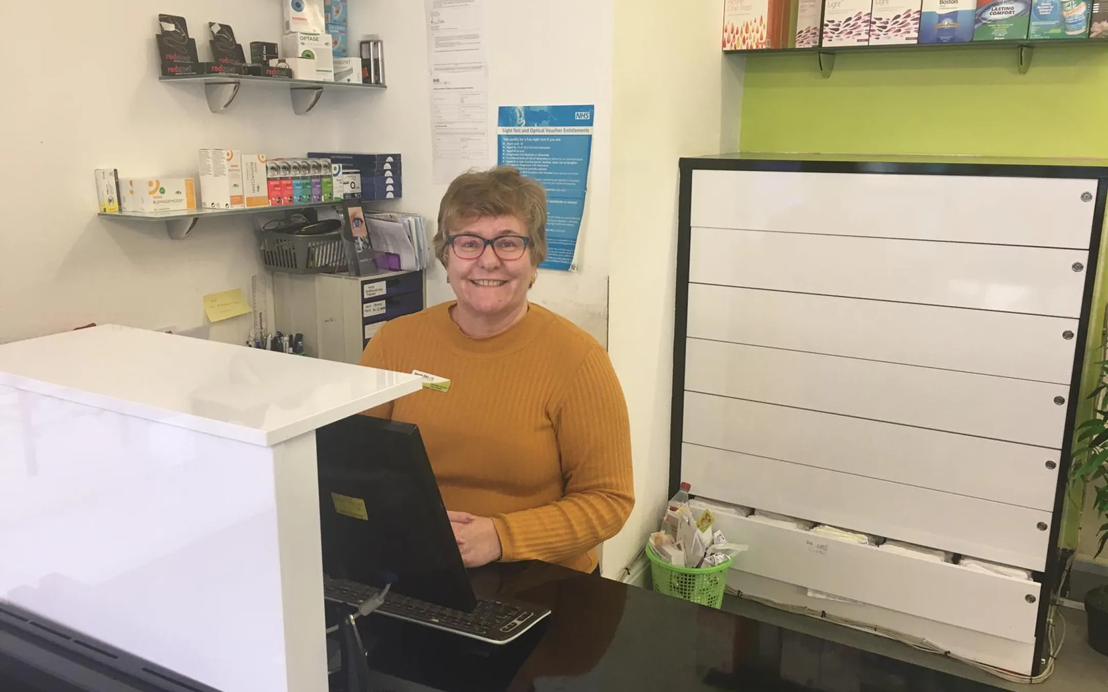 Friendly opticians reception desk staff welcoming patients for eye appointments