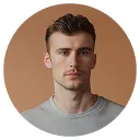 Portrait of a young man with short brown hair and a trimmed mustache and beard wearing a gray shirt against a brown background.