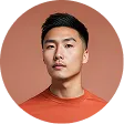 Portrait of a young Asian man wearing an orange shirt against a peach background.