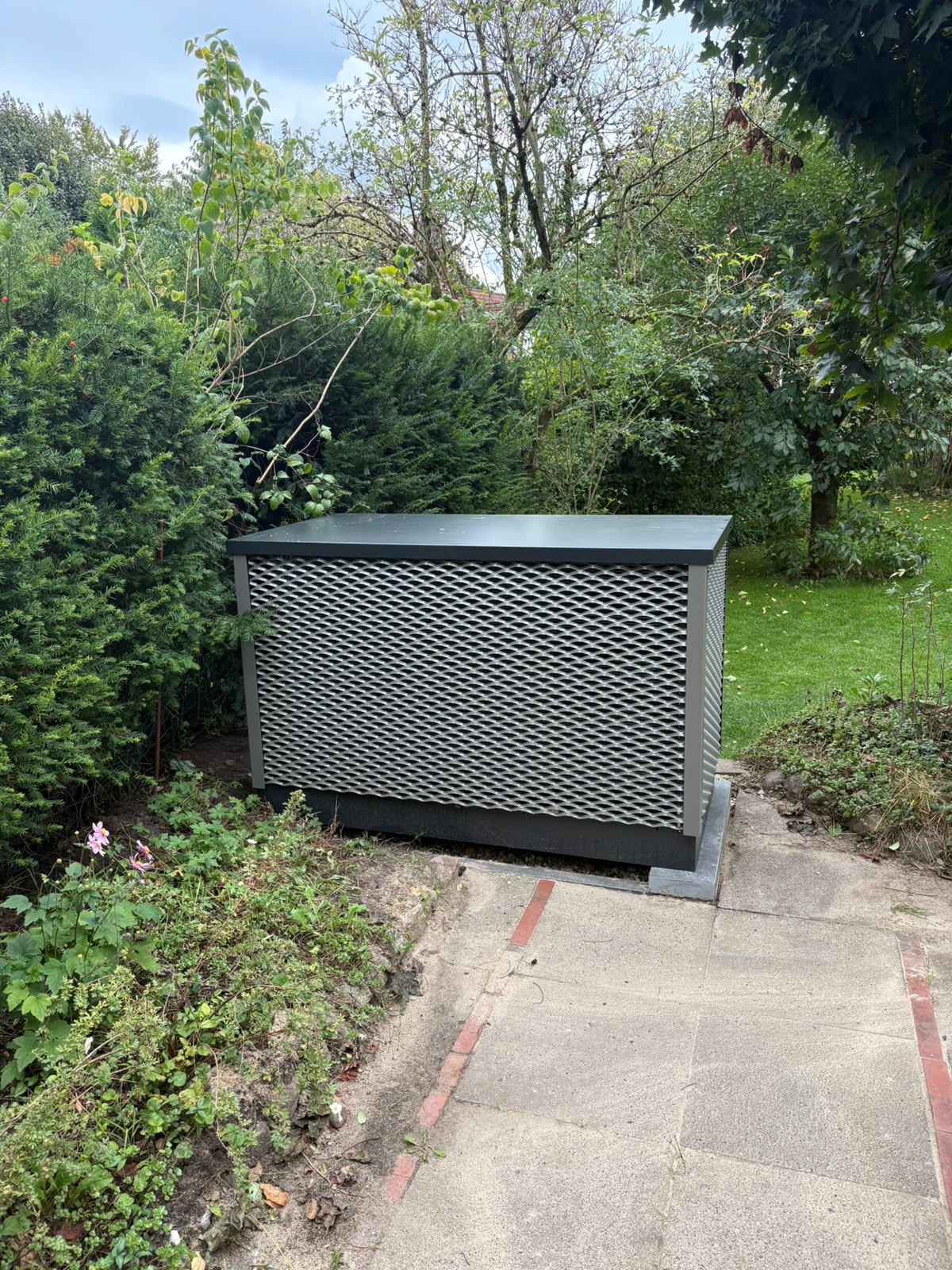OVUM Wärmepumpe mit Streckmetall-Verkleidung vor einer Hecke im Garten