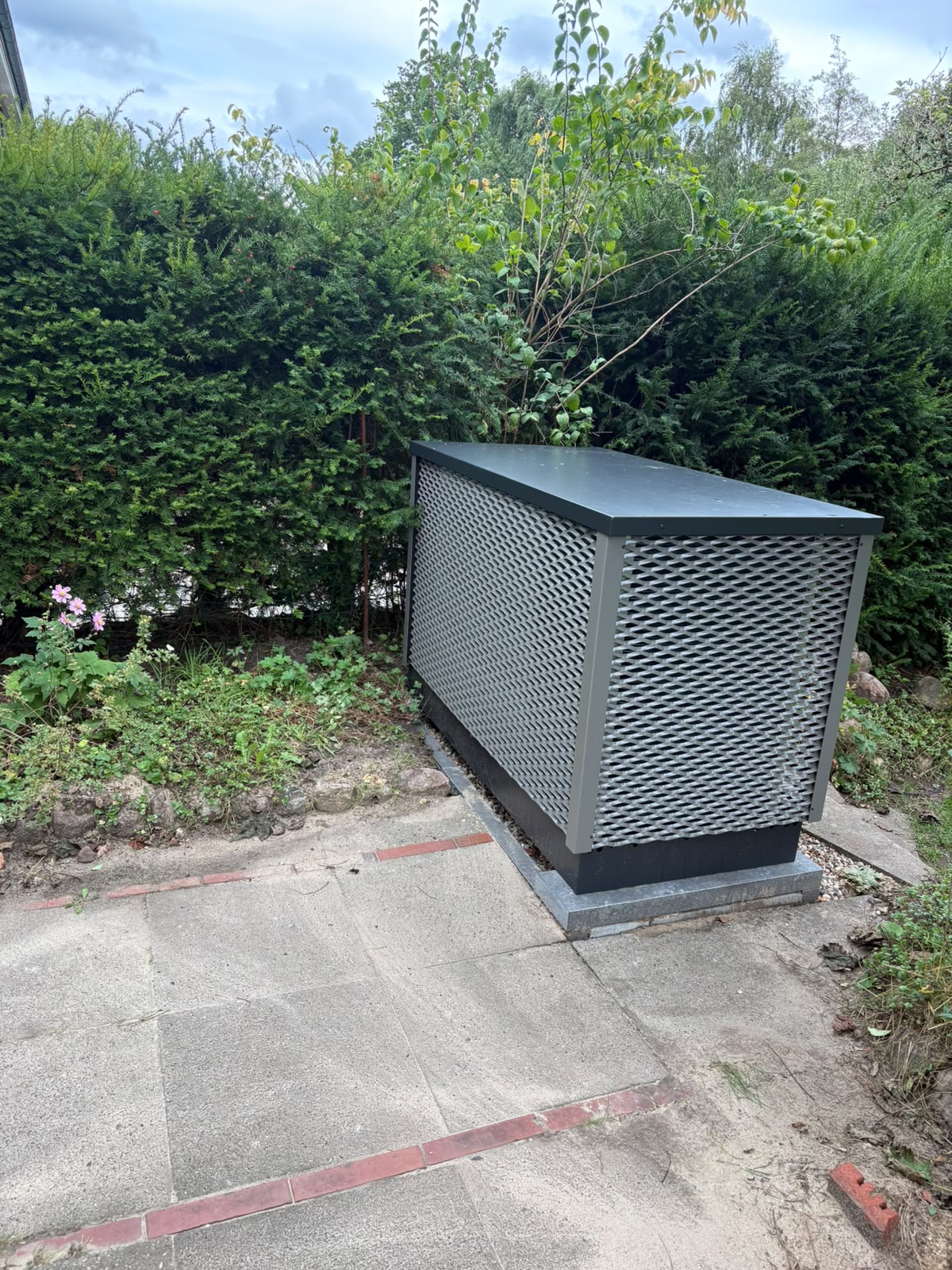 Seitenansicht der OVUM Wärmepumpe auf Fundament, Leitungen unsichtbar unter dem Gerät angeschlossen