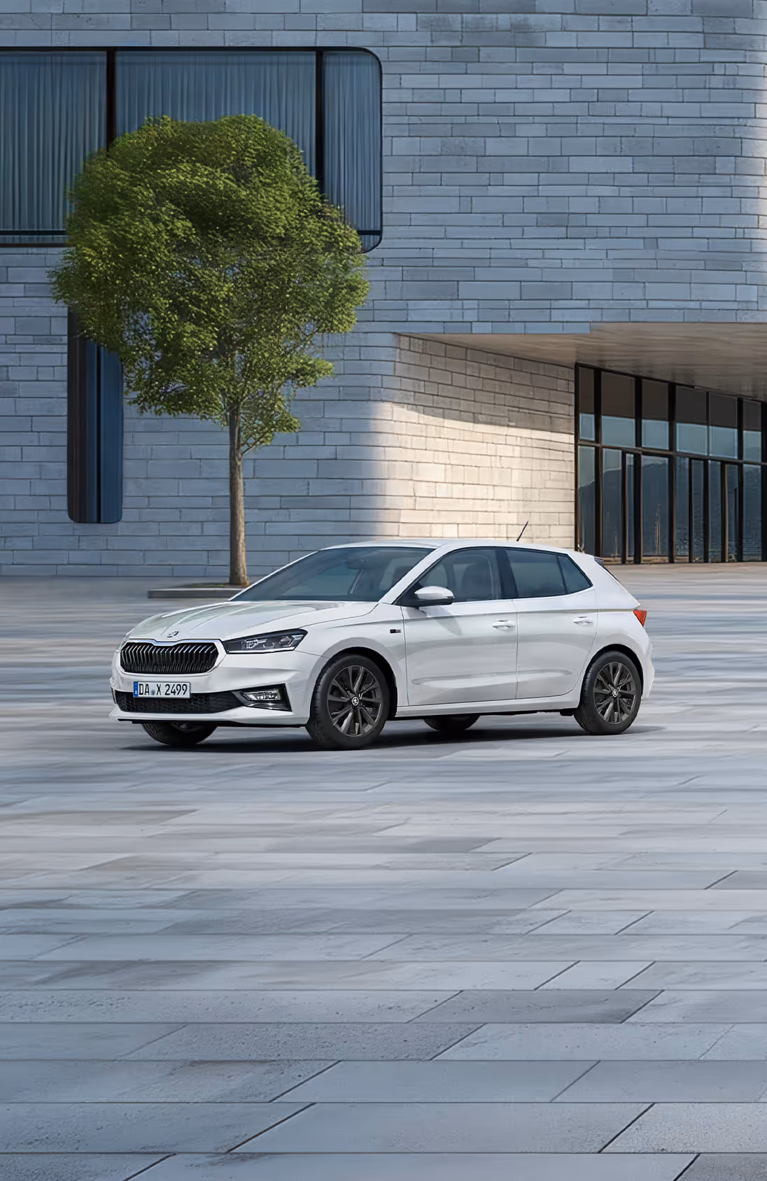 Seitenansicht eines Škoda Fabia Balance in der Lackierung Moon-Weiß Perleffekt vor einer modernen, grauen Gebäudefassade. Das Fahrzeug ist mit dunklen 16-Zoll-Leichtmetallfelgen Proxima (schwarz glanzgedreht) ausgestattet. Auf dem Bild ist ein grüner Störer platziert, der einen Preisvorteil in Höhe von 1.800€ sowie 5 Jahre Garantieleistung bewirbt. 