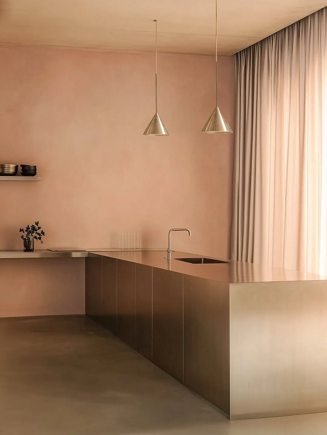 Schneid Studio Figura pendant lights, a pair of sleek brushed metal cone fixtures suspended over a minimalist stainless steel kitchen island against dusty pink plaster walls.