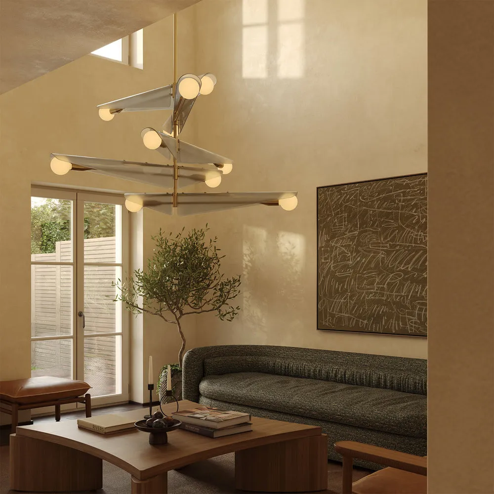 Tala Sycamore 5-Tier Chandelier, a modern architectural fixture with angled dawn grey panels and frosted globe bulbs, suspended in a warm, double-height living room featuring a curved grey textured sofa, a wooden coffee table, and an indoor olive tree.