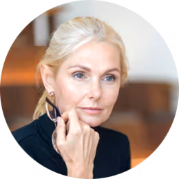 Kvinna i svart blazer med blont hår som vilar handen mot kinden