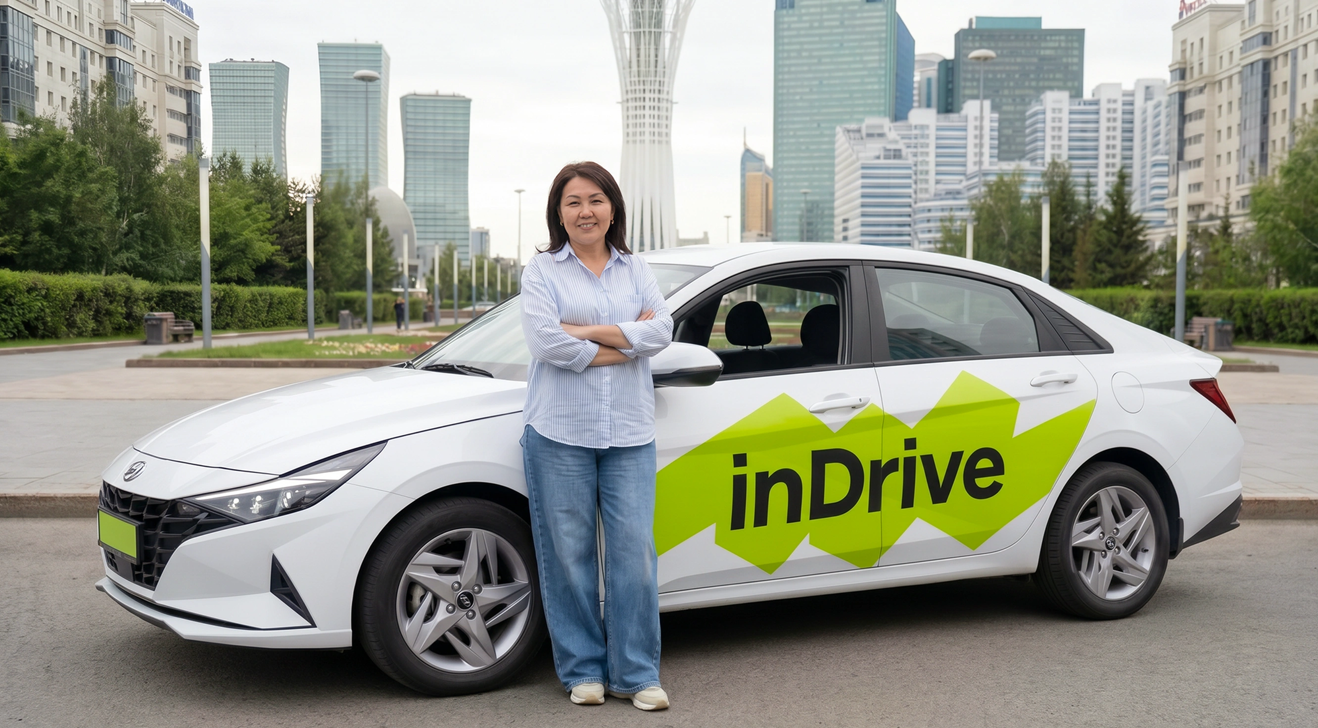 Woman with crossed arms standing beside a white sedan with a large green 'inDrive' logo on the side, in an urban area with tall buildings and greenery in the background.