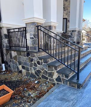 Stone staircase with black metal railing outside a building with white columns.