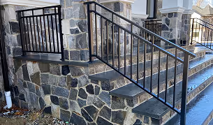 Stone staircase with a black metal railing attached to a building with a stone facade and white trim.