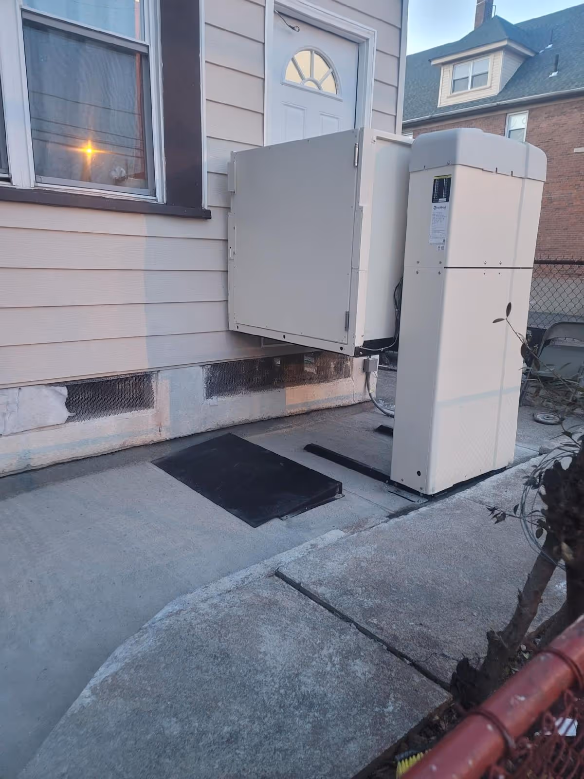 Outdoor residential wheelchair platform lift installed next to a house door with a small ramp and control panel.