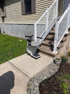 Outdoor stairlift installed on concrete steps leading up to a porch with beige siding and white railings.