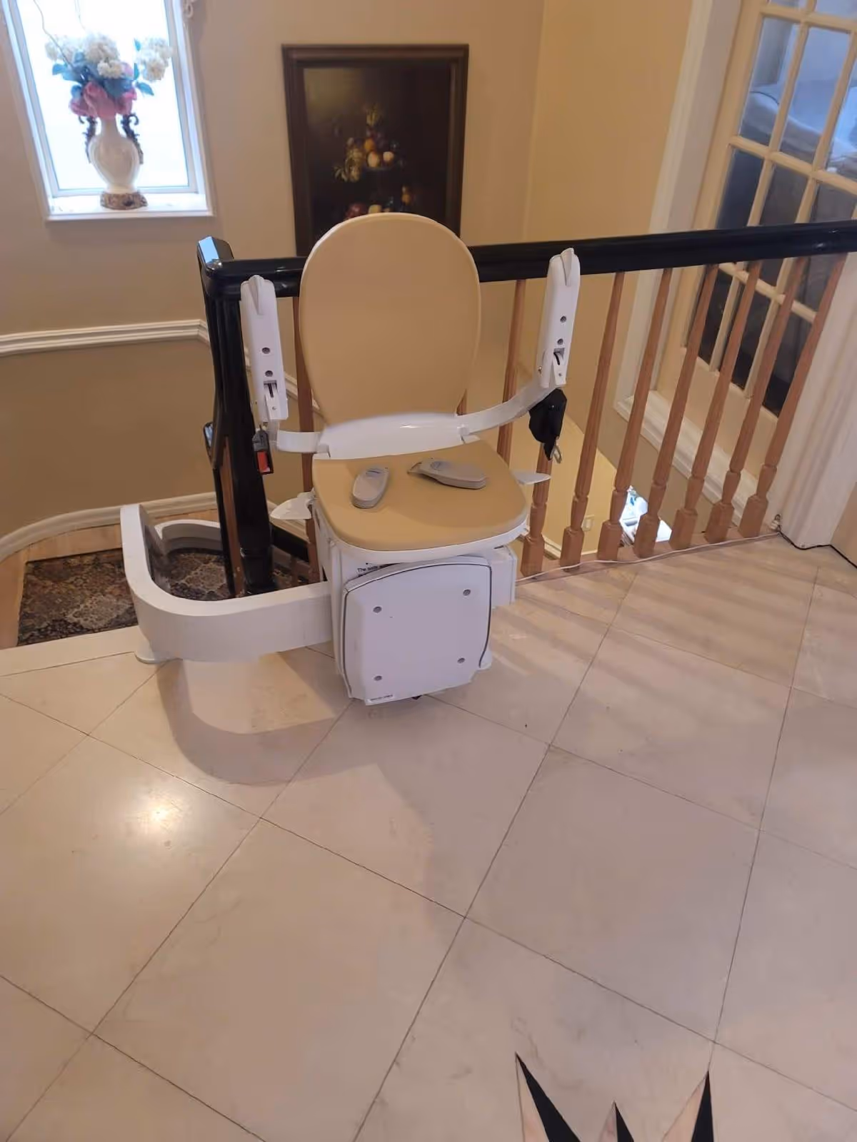 Beige and white stairlift installed on a curved staircase railing inside a home.
