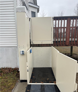 Stiltz home lift with glass doors installed indoors next to a white bookshelf and black chair.