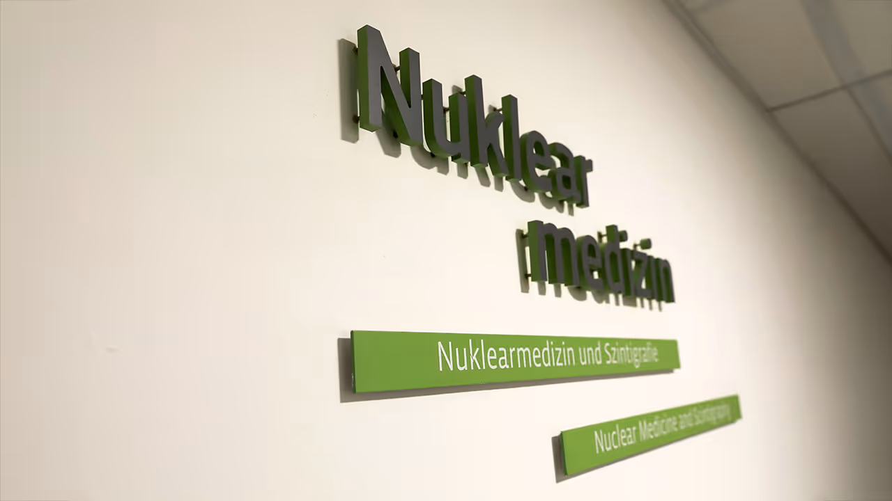 Green 3D letters on a white wall display “Nuclear Medicine” and similar terms, indicating a nuclear medicine department.