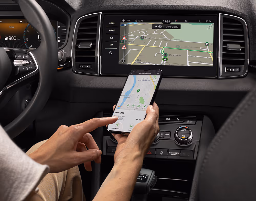 Innenraumansicht des Škoda Karoq Balance, in der eine Person ihr Smartphone mit dem Infotainment-System verbindet. Auf dem zentralen Touchscreen ist die Benutzeroberfläche von Apple CarPlay mit verschiedenen App-Icons zu sehen. Das Bild veranschaulicht die Smartphone-Integration im Fahrzeug.