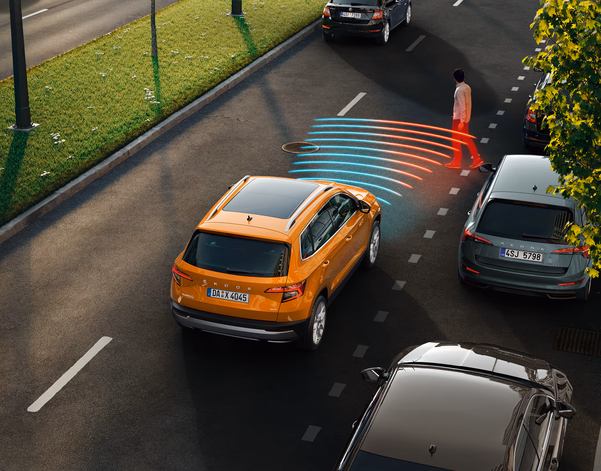 Animation des Frontrad- und Ausweichassistenten. Ein orangefarbener Škoda Karoq Balance fährt die Straße entlang. Plötzlich überquert ein Fußgänger, der aus einem schwer einsehbaren Bereich kommt, die Straße. Das System warnt.