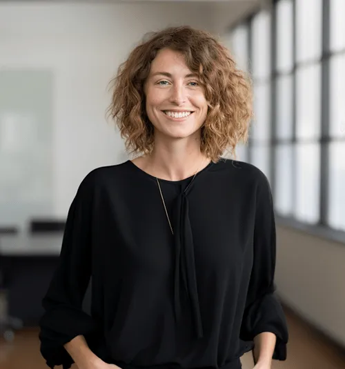 Smiling woman with curly light brown hair wearing a black blouse in a bright office space.