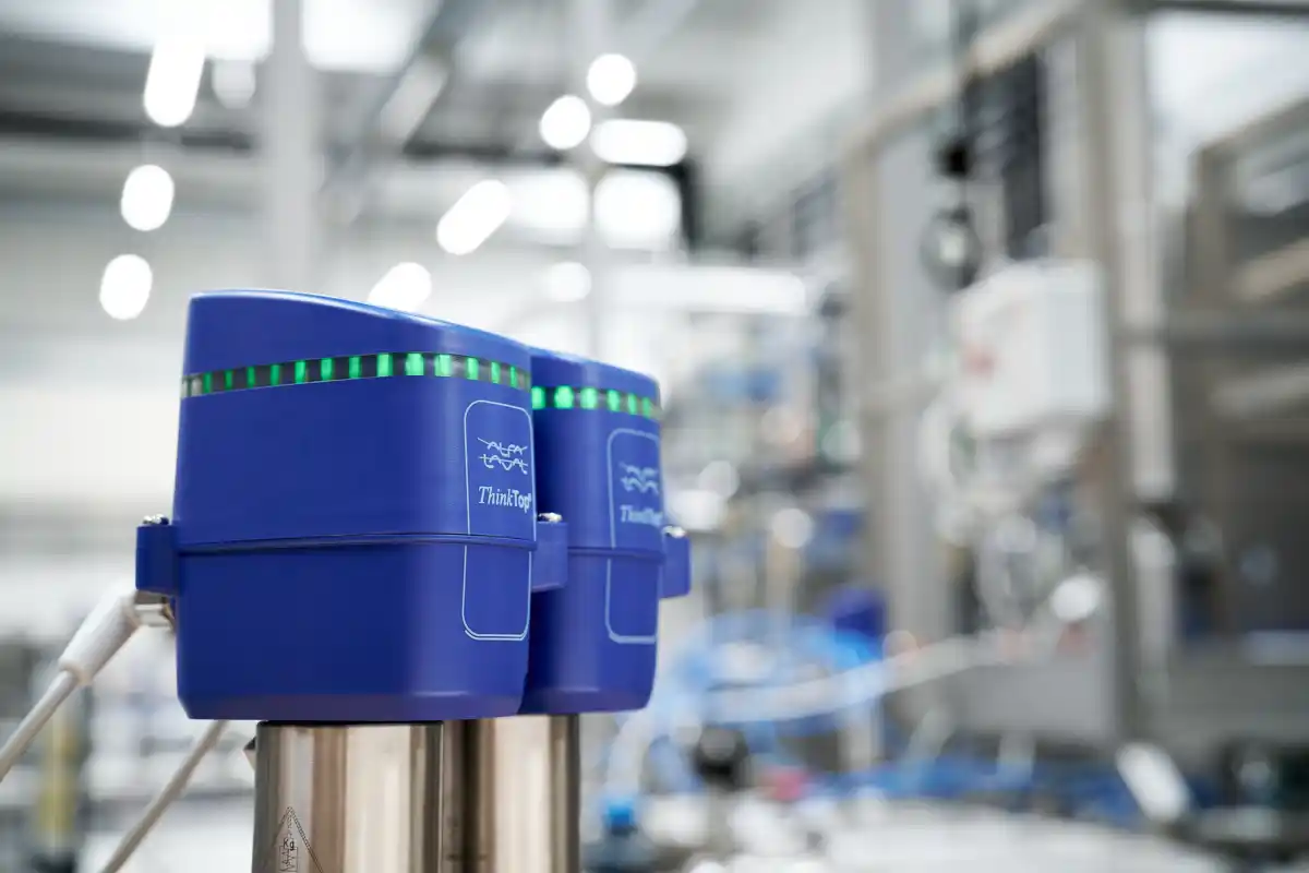 To blå industrielle sensorer merket ThinkTop med grønne lys i en fabrikksetting.