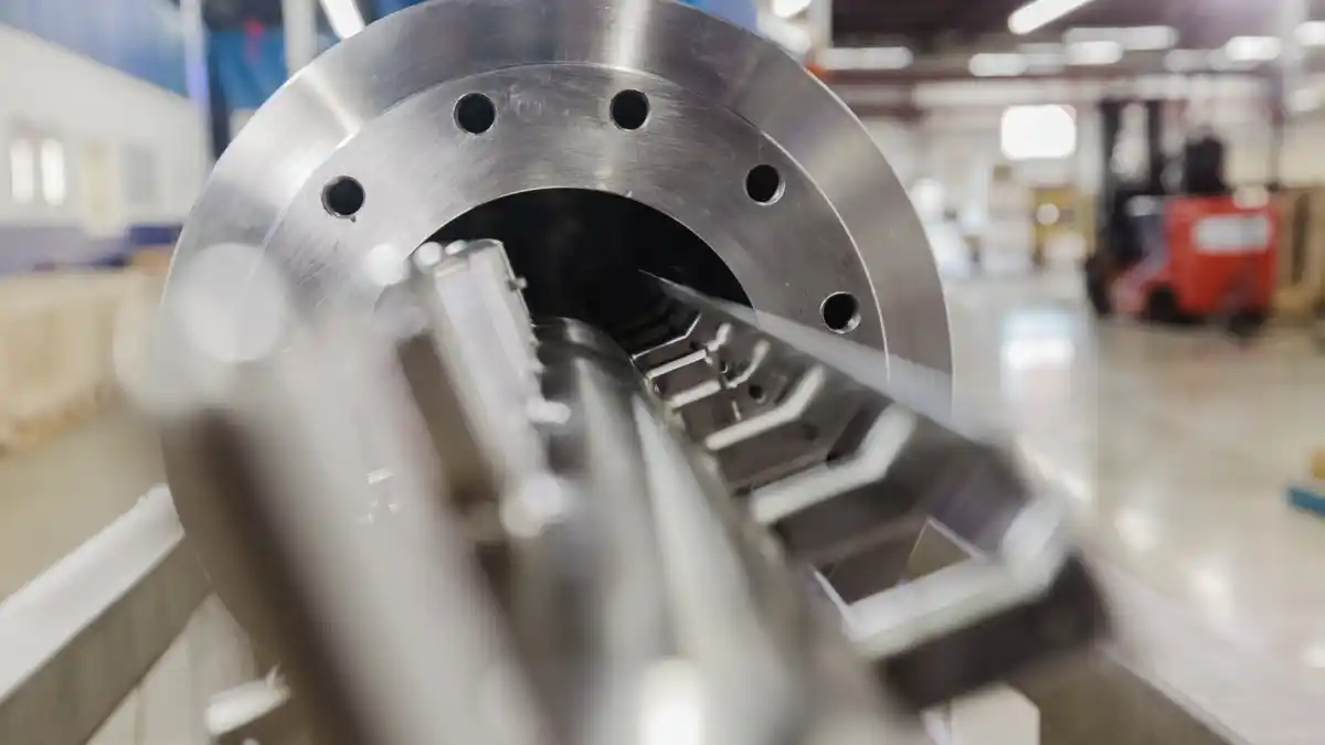 Nærbilde av metallkomponent med hull og gjenger i et verkstedmiljø.