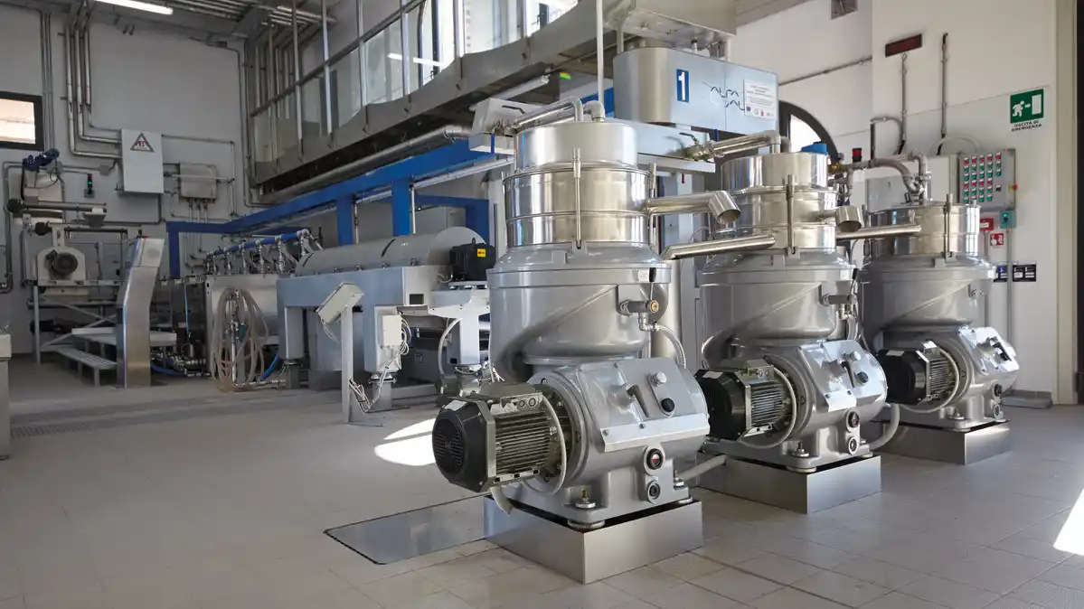 Industrielt rom med tre store, metalliske maskiner til oljeforedling på gulvet og flere maskiner i bakgrunnen.