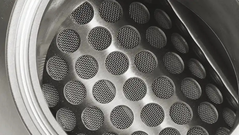 Nærbilde av et metallfilter med runde hull dekket av fint nett.