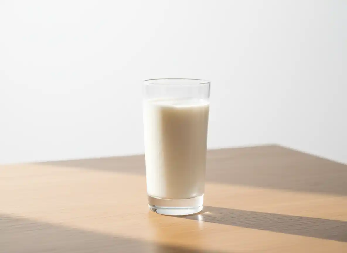 Et glass melk på et lyst trebord med skygge.