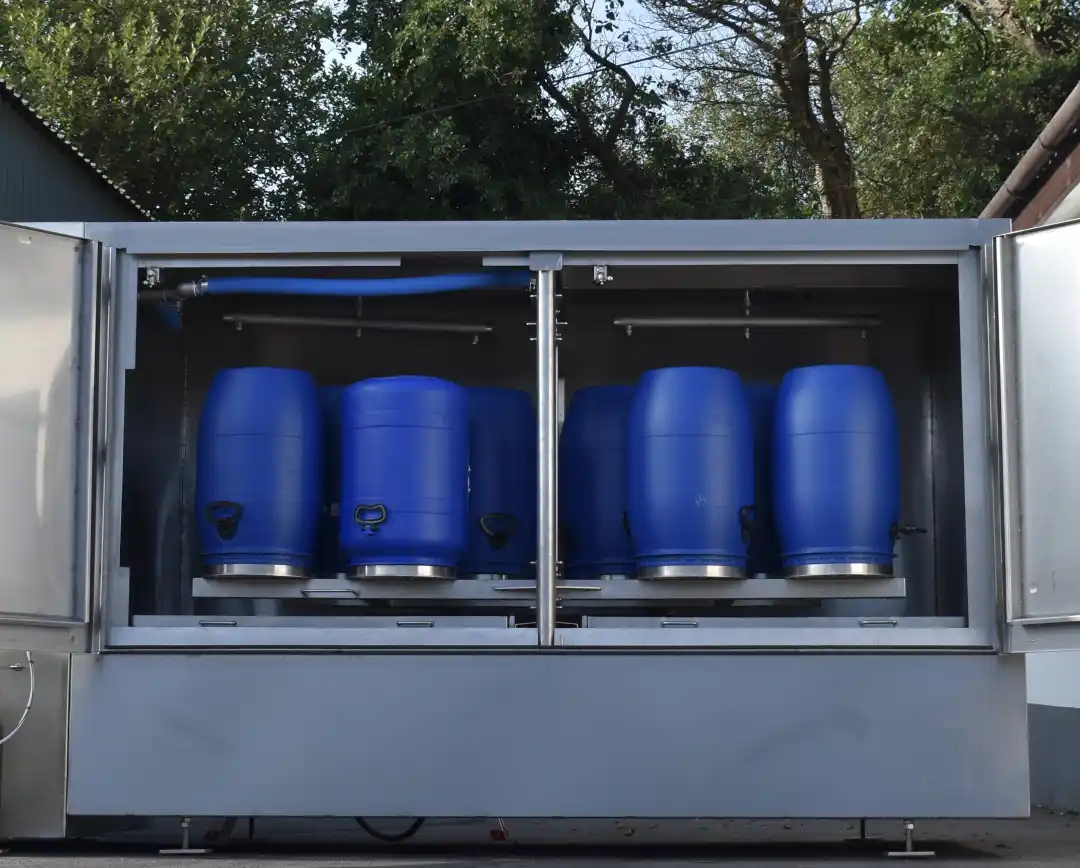 Automatisk rengjøringsmaskin med flere blå plasttønner plassert inne i et grått metallskap utendørs.