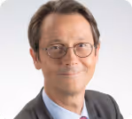 Homme portant des lunettes et un costume avec une cravate, souriant légèrement.