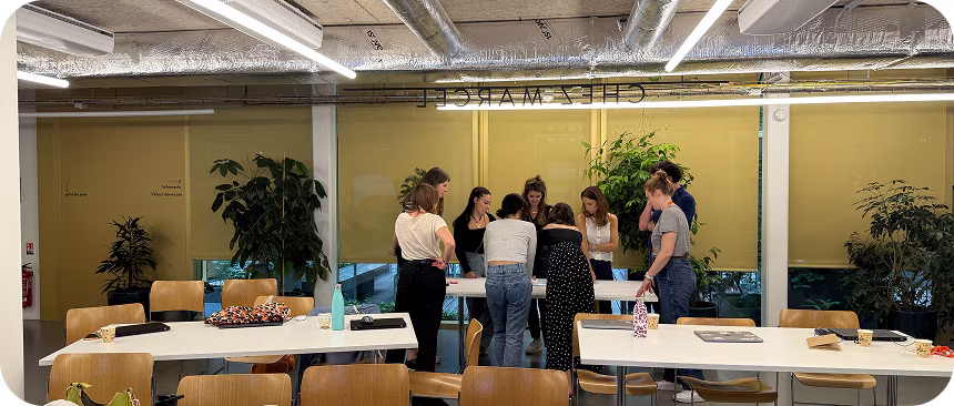 Un groupe de huit personnes debout autour d'une table blanche dans une salle de réunion moderne avec des chaises en bois et des plantes.