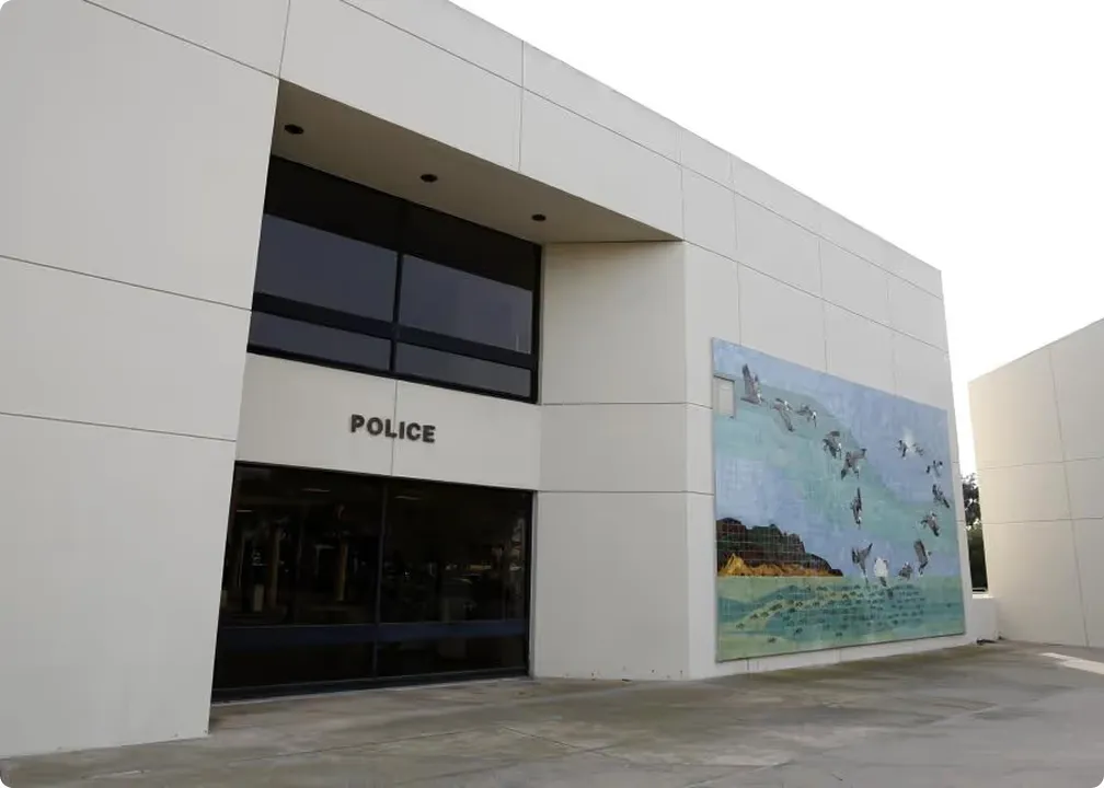 Modern white building with black glass doors labeled 'POLICE' and a large mural featuring flying birds over a coastal landscape.