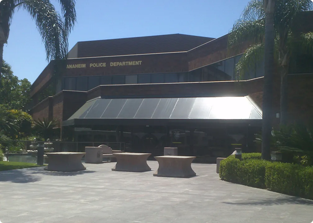 Exterior of Anaheim Police Department building with palm trees and outdoor benches in front.