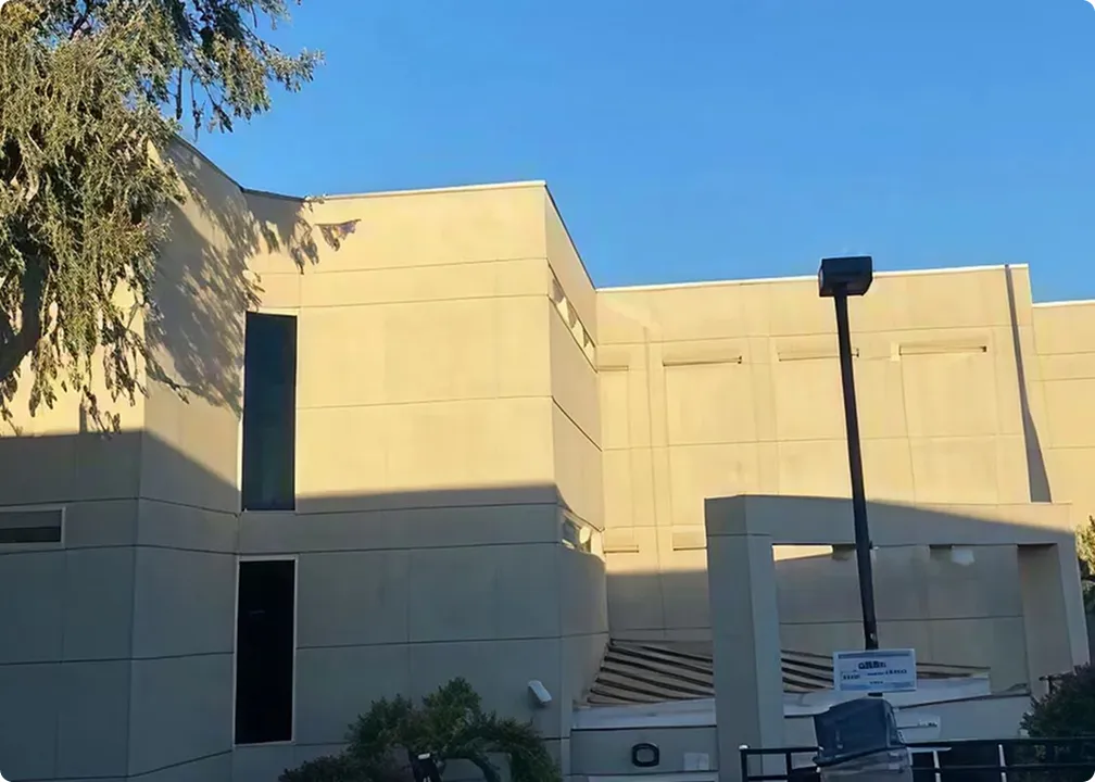 Exterior of a beige multi-story building with vertical windows, a streetlight, and clear blue sky.
