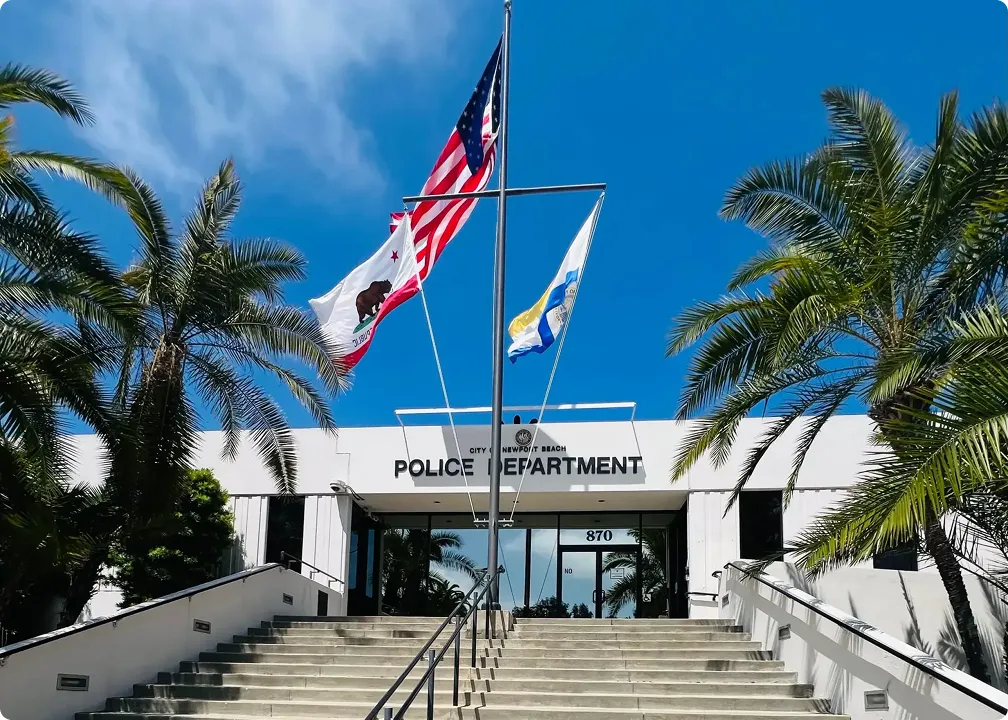 Entrance of Newport Beach Police Department building with flags flying and palm trees on each side.