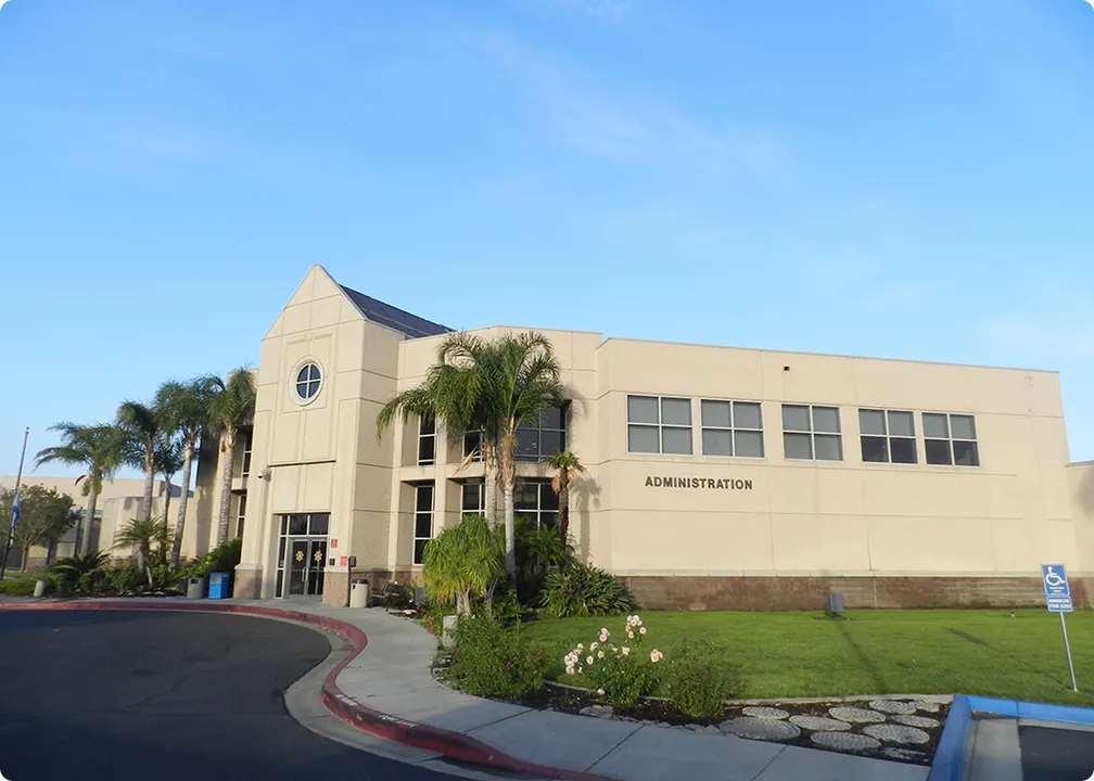 Modern beige administration building with palm trees, green lawn, and clear blue sky.